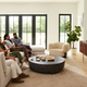 A group of four people sitting on a sofa watching a TV with the JBL Bar 1300X soundbar located beneath the TV and the detachable speakers positioned behind them.